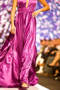 Modelka na wybiegu w długiej rozkloszowanej sukni z satyny jedwabnej koloru fuksji